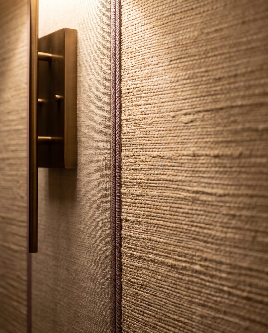 Textured grasscloth wall detail with a clean seam and bronze wall sconce